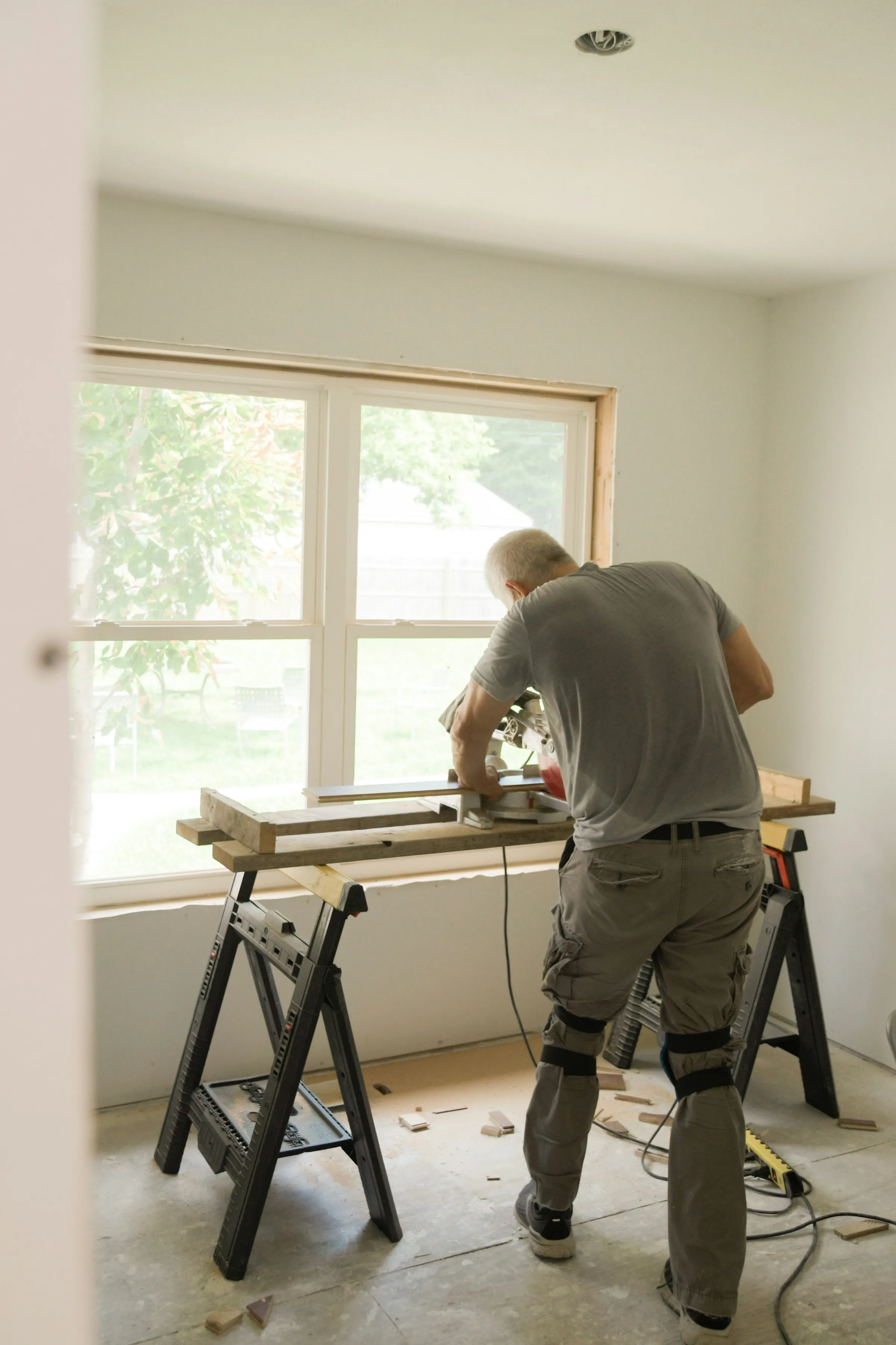 Menuisier au travail dans une pièce en rénovation, devant une grande fenêtre